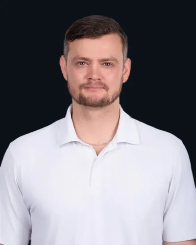 Portrait of the person behind A7A, in a white polo shirt against a dark navy background